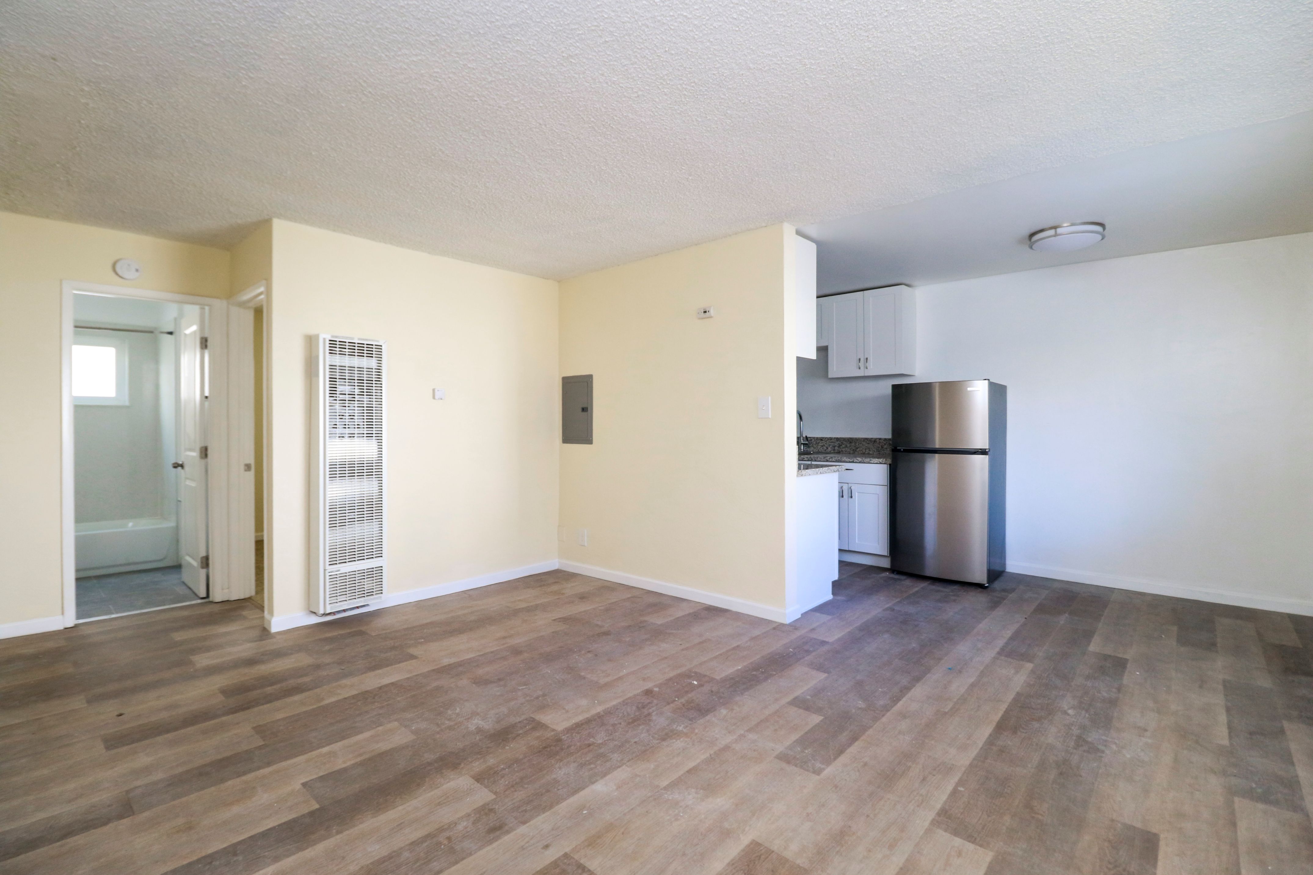 A room with wooden flooring and a stainless steel refrigerator.